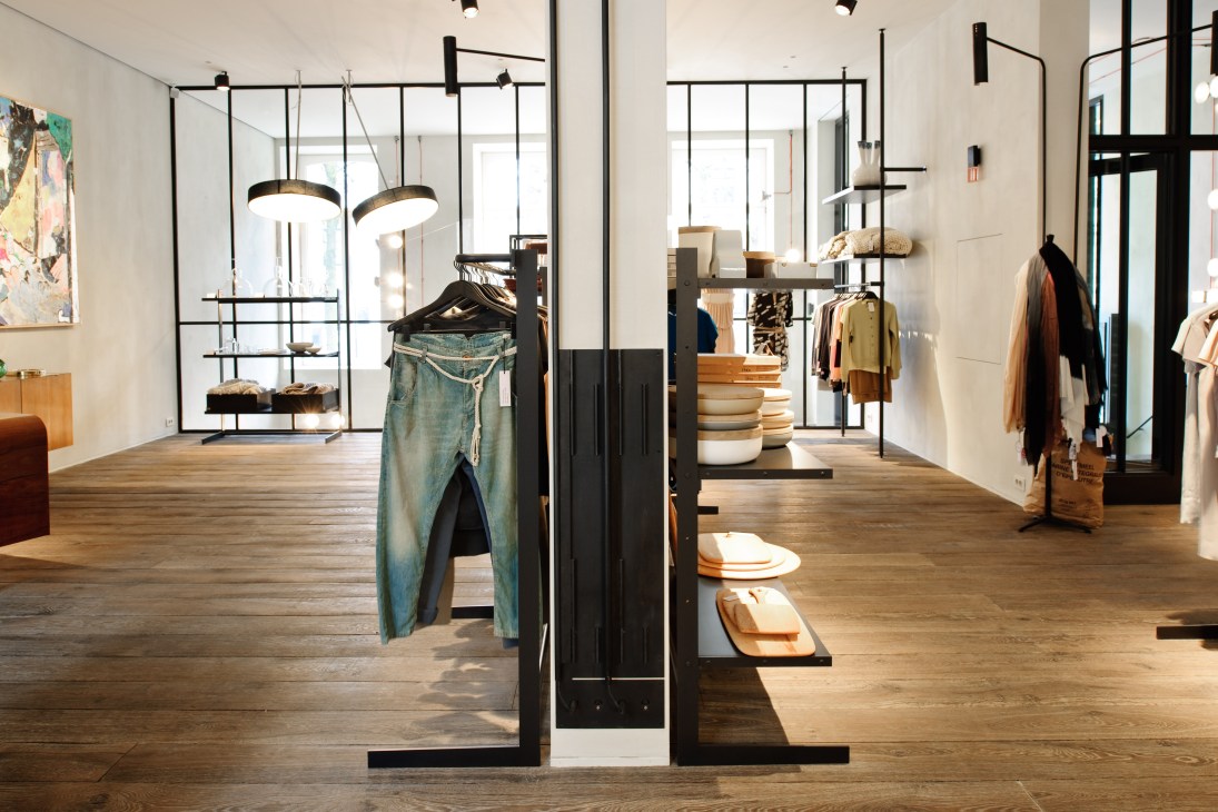 Interior of Graanmarkt 13 retail store in Antwerp with minimalist design, black metal fixtures, wooden flooring, and clothing displays.