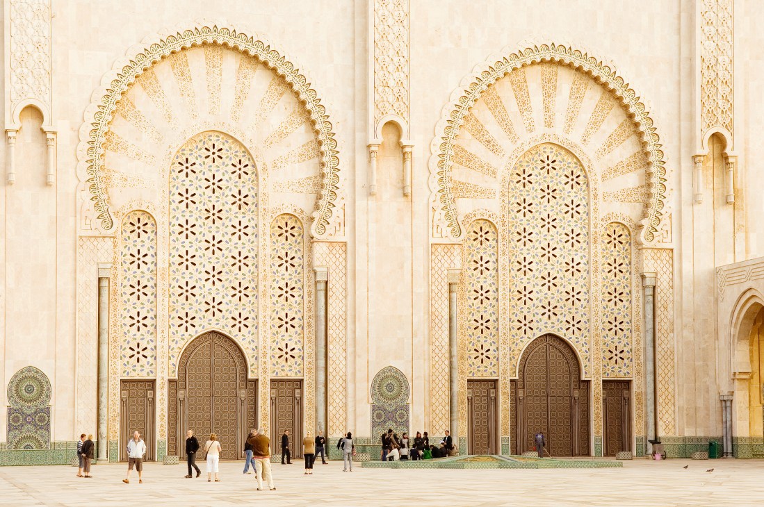 Mosque Hassan II's ornate facade featuring two large arched doorways with geometric patterns and decorative tilework in cream and gold tones.