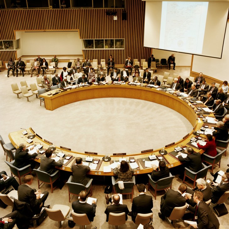 UN Security Council chamber with delegates seated around curved wooden table during formal session