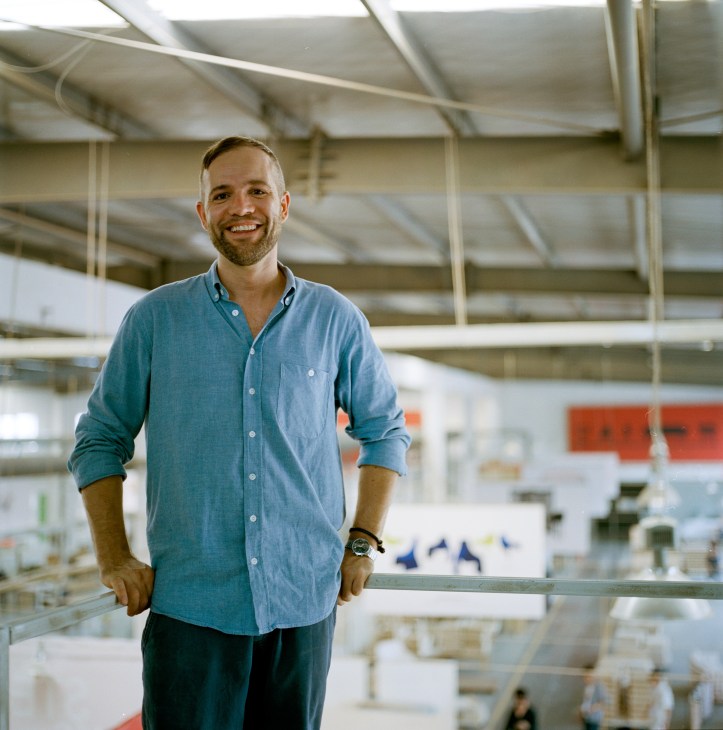 Thomas Lykke, creative director of OeO, stands in a furniture factory wearing a blue shirt.