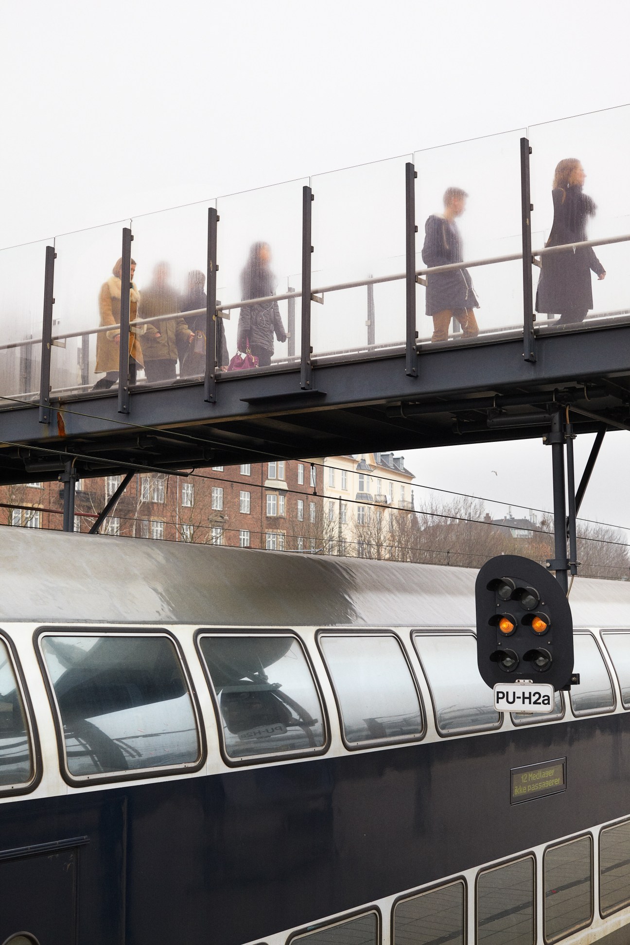 Commuters walking across an elevated pedestrian bridge above a train at Østerport station in Copenhagen.
