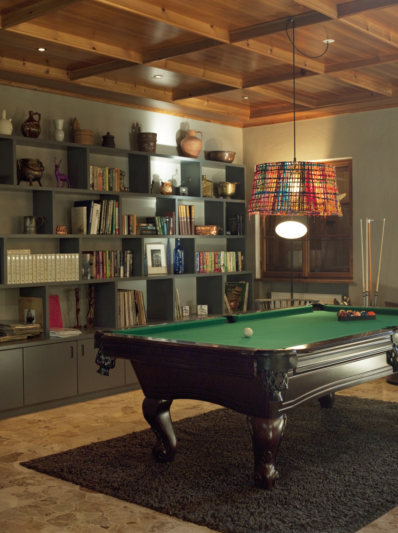 Modern game room with billiard table, wooden ceiling beams, and built-in shelving.