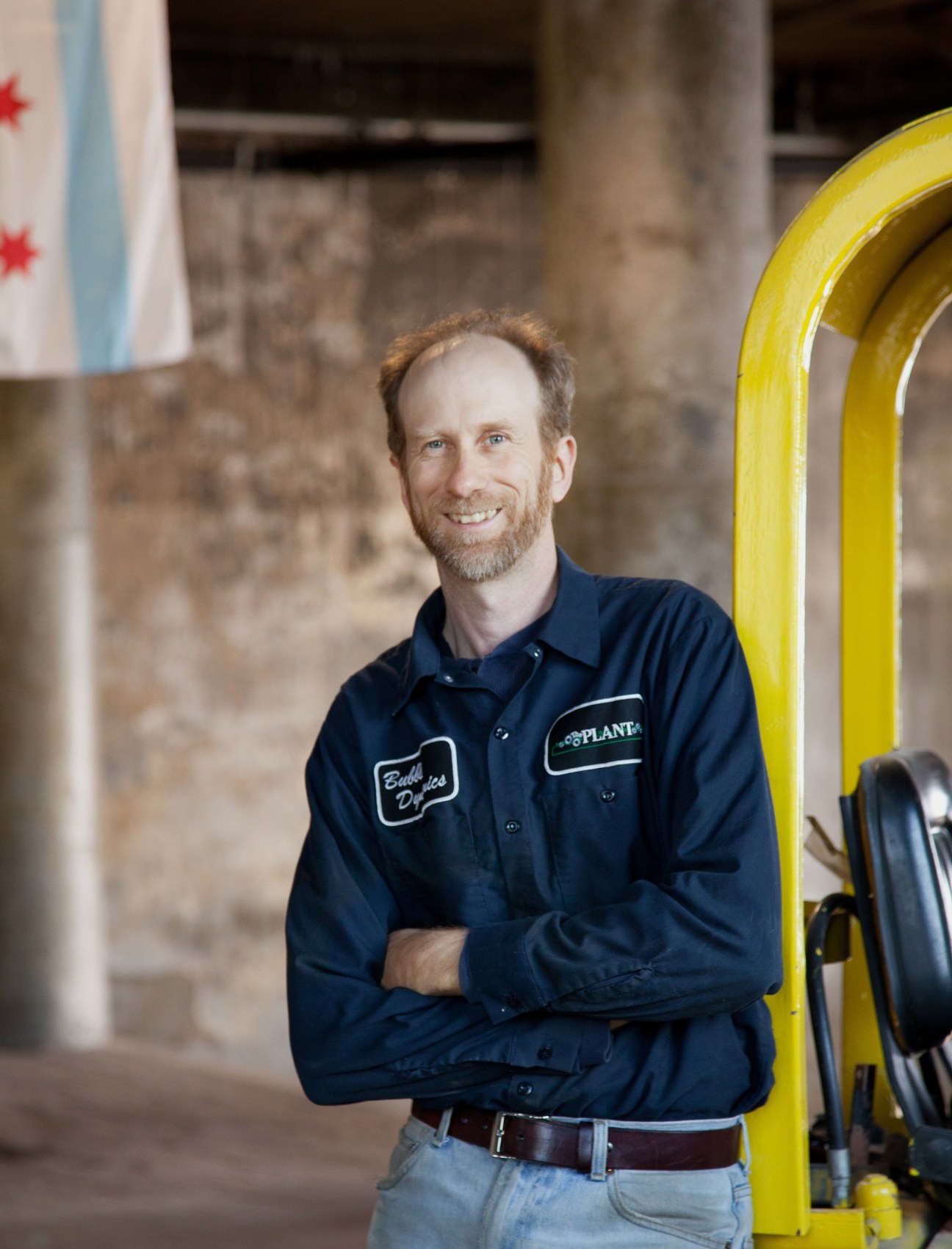 Man in navy work shirt with The Plant logo standing next to yellow industrial equipment in warehouse