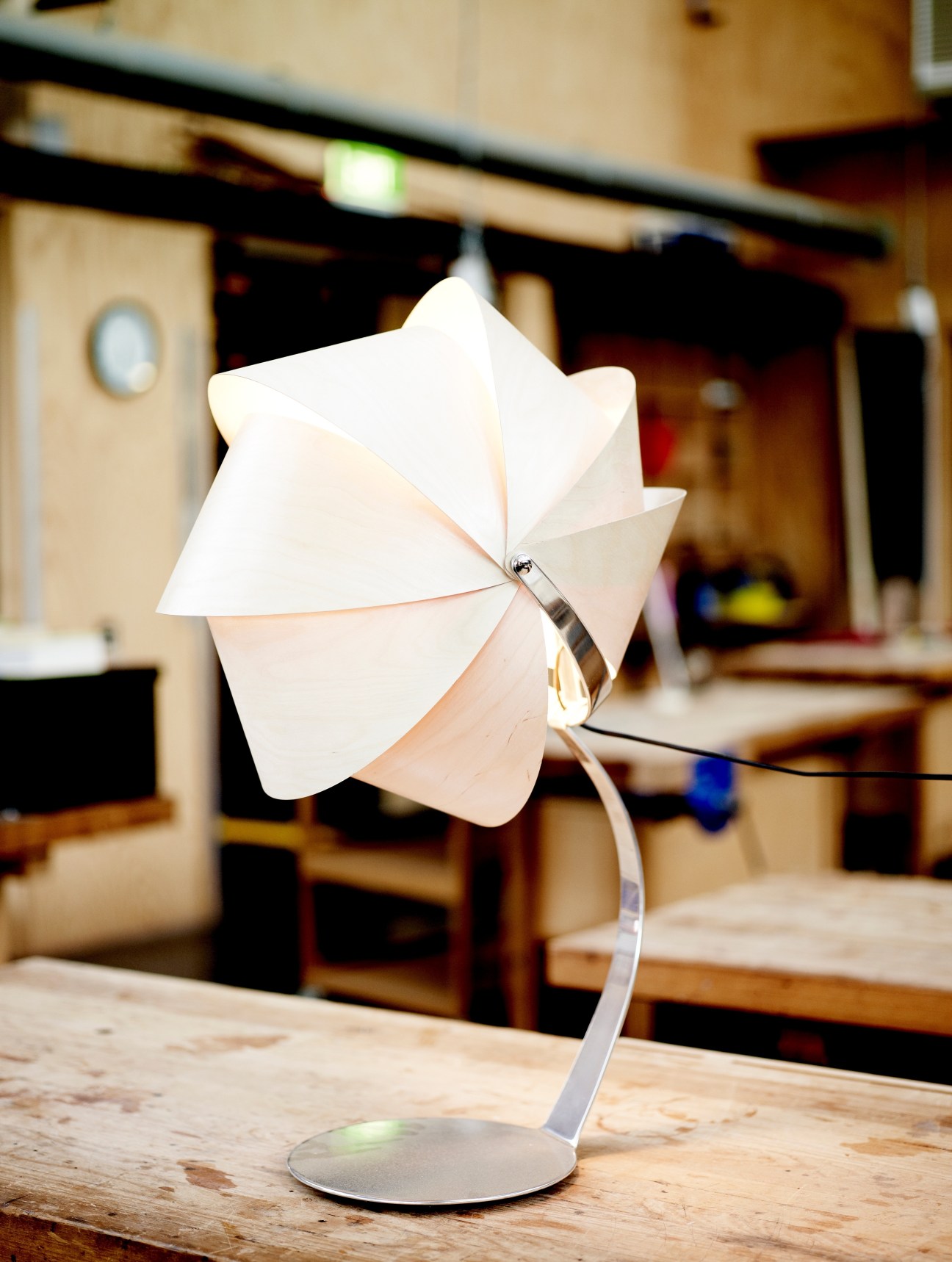White origami-style lamp with geometric folded panels on a metal stand in a workshop.