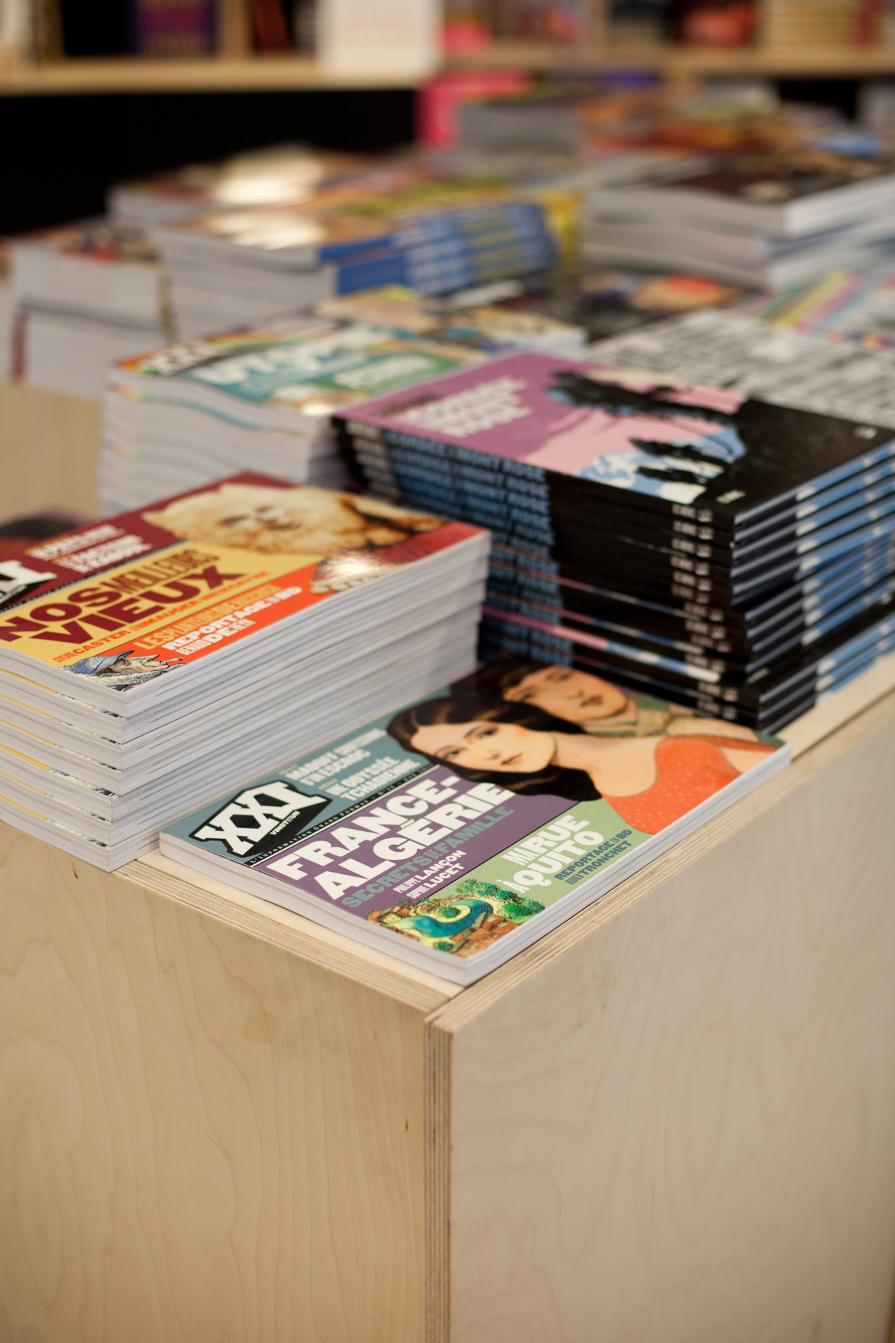 Stacks of colorful magazines displayed on a wooden table in a bookshop.