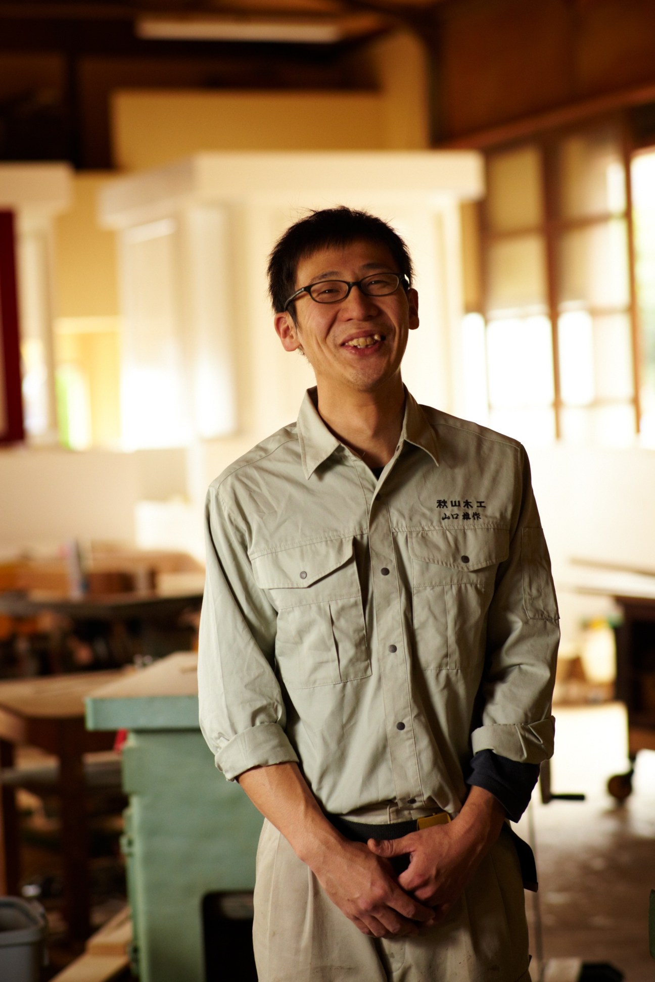 Yusaku Yamaguchi, 26-year-old shokunin at Akiyama Mokko furniture workshop, smiling in workshop interior