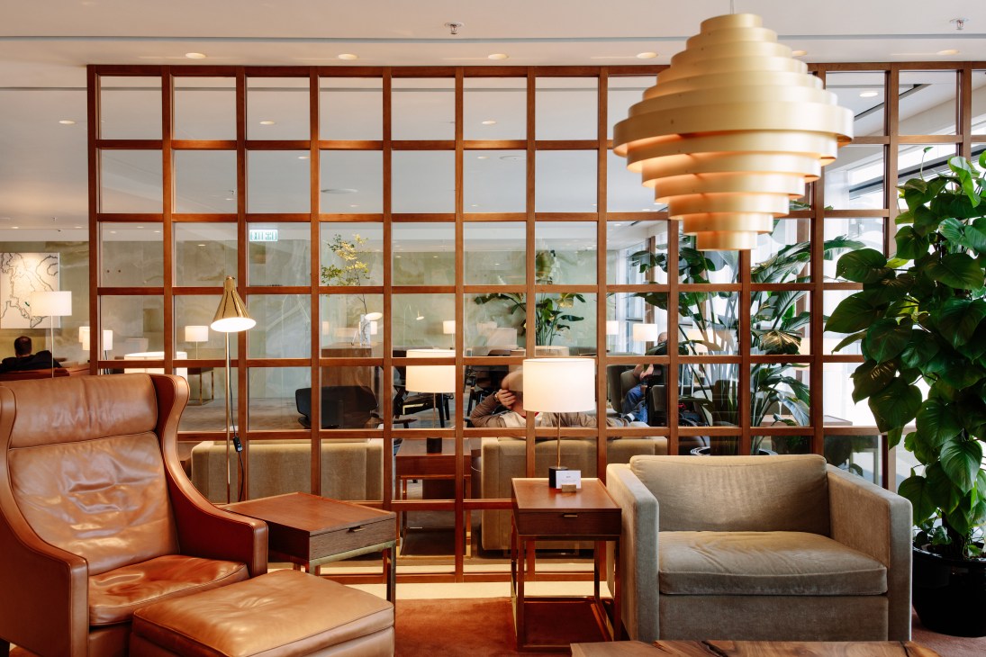 Modern airport lounge interior with leather seating, golden pendant lamp, and gridded wooden partition wall.