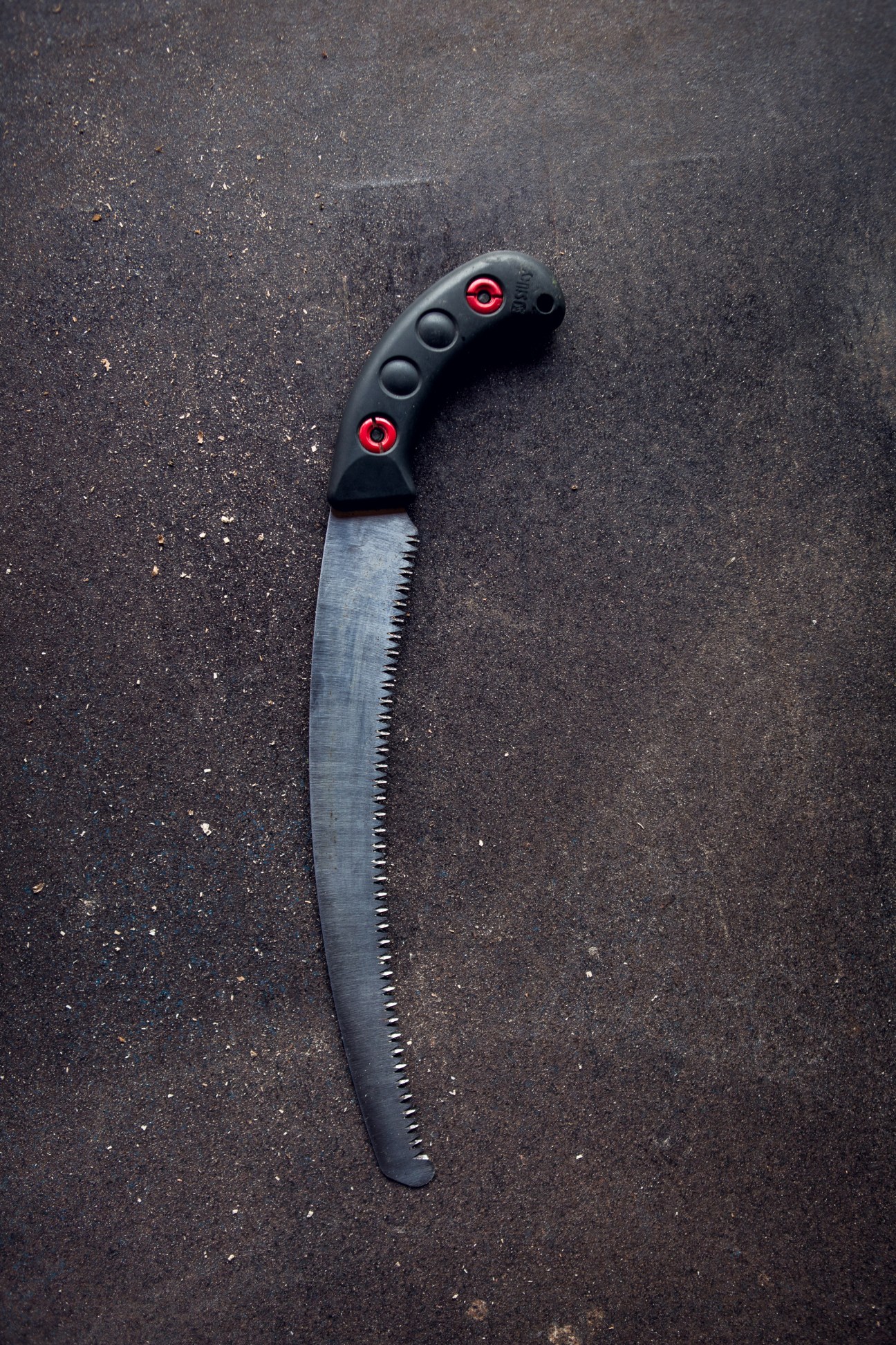 A coppicing saw with a black handle and red accents on a dark textured surface.