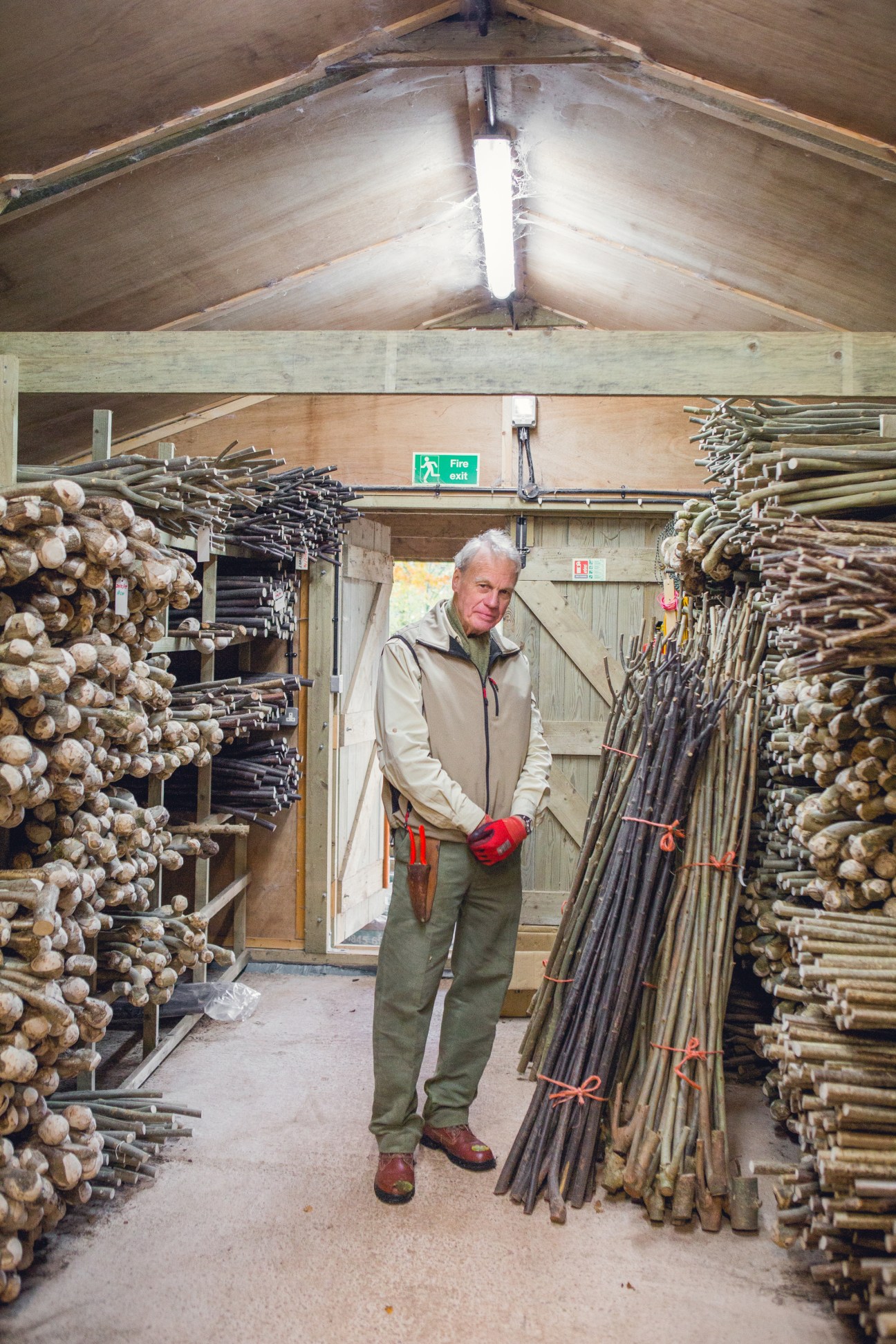 Founder Ben Porter stands in Classic Canes workshop surrounded by stacked wooden cane materials.