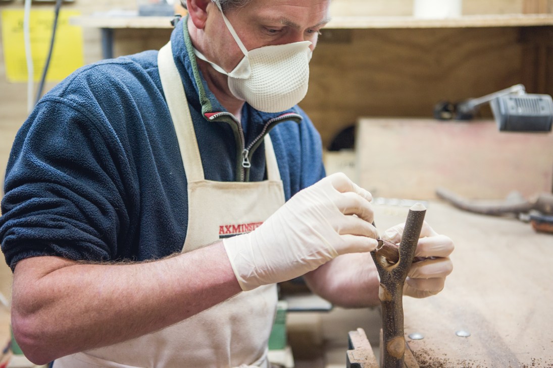 Craftsman hand finishing a walking stick with tools in a workshop.