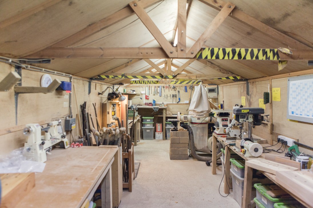 Interior of Classic Canes workshop showing wooden workbenches, machines, and tools organized under exposed beams with yellow and black safety striping.