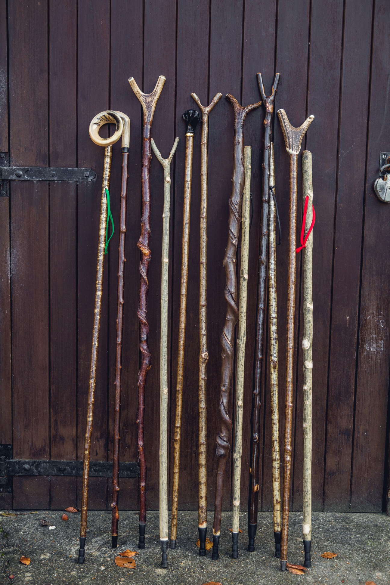 Collection of finished walking sticks with varied natural wood finishes and decorative handles leaning against a dark wooden wall.