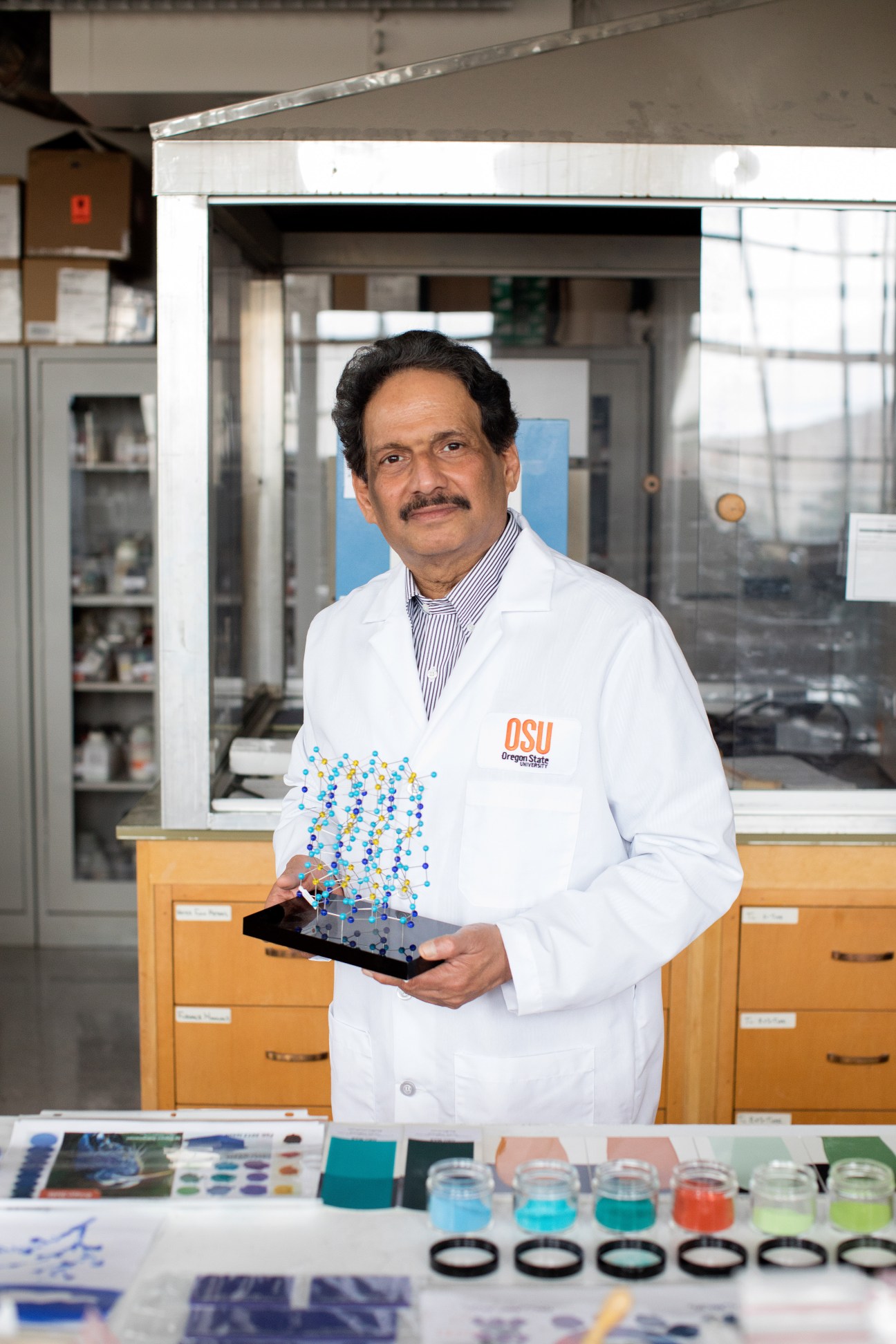 Man in OSU lab coat holding a blue molecular structure model in a laboratory setting.