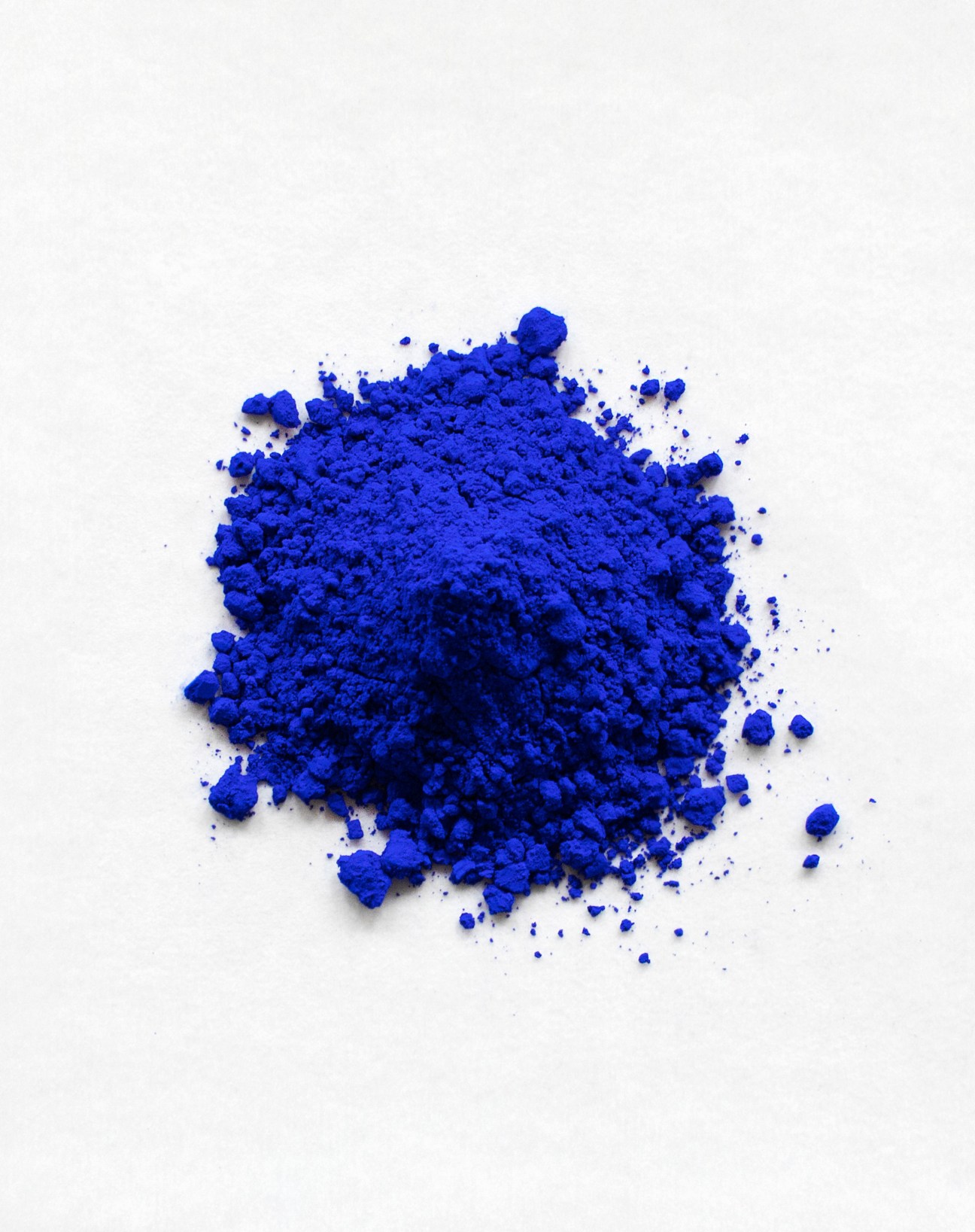Bright blue YInMn pigment powder scattered on a white surface.