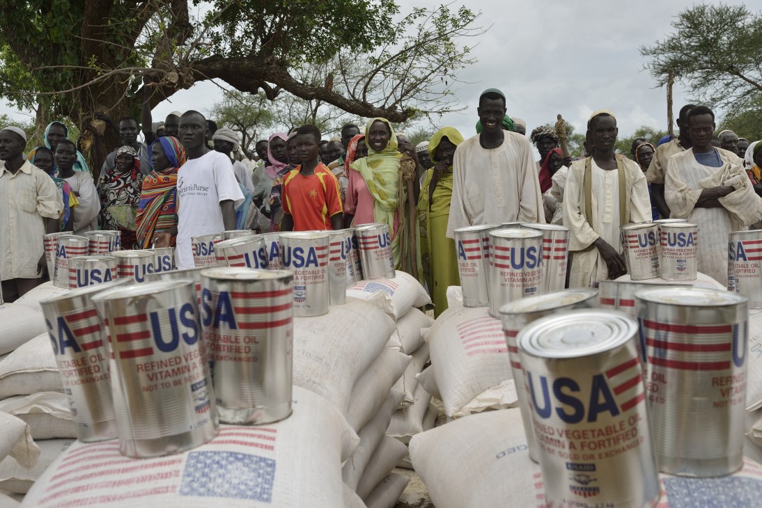Refugees queue for food distribution at Batil camp with USAID containers and supplies visible.