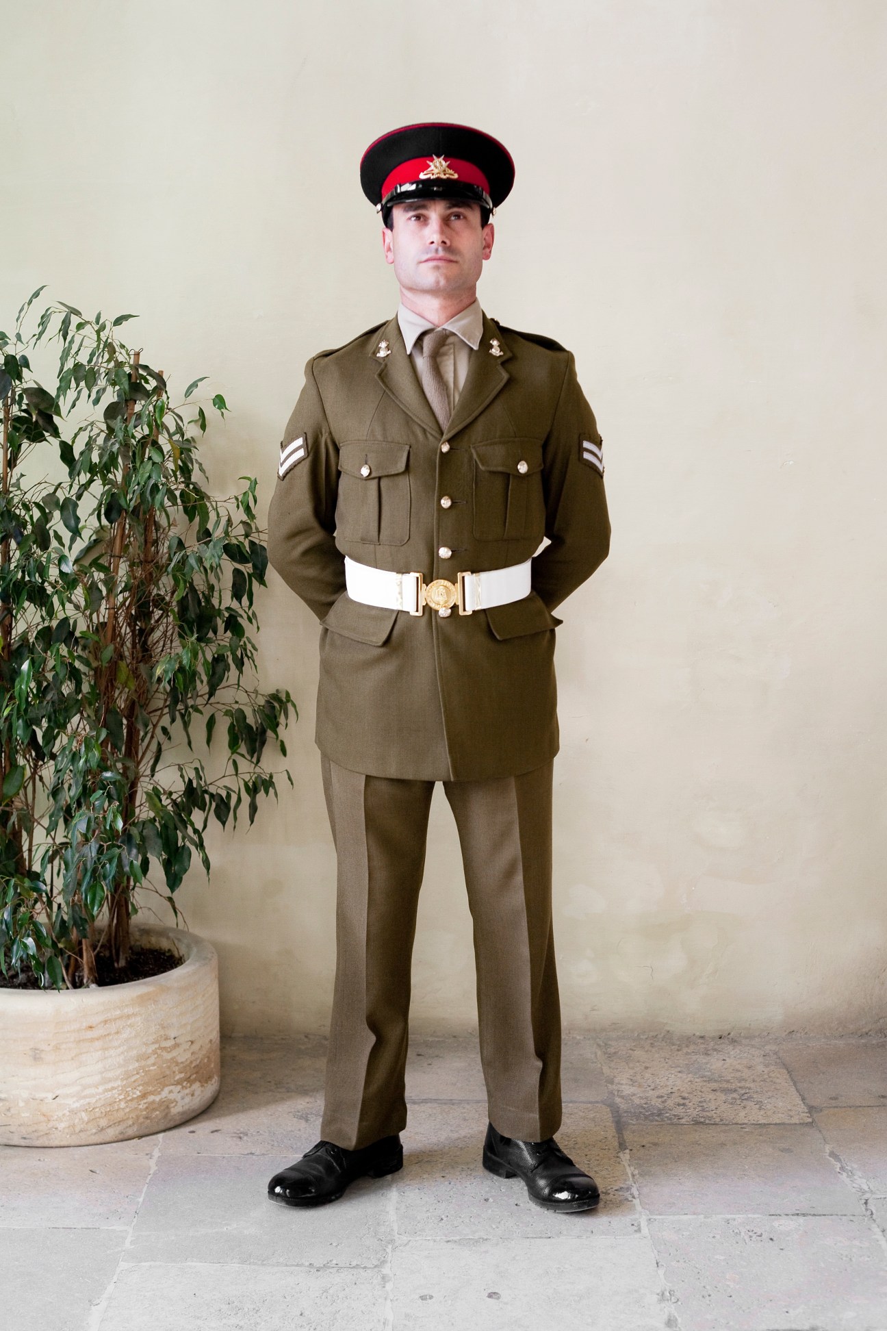 Guard in brown military uniform with red cap standing inside the Auberge de Castille.