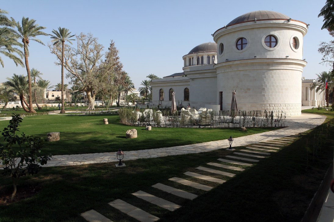 Modern white domed building with circular windows surrounded by manicured gardens and palm trees in Jericho.
