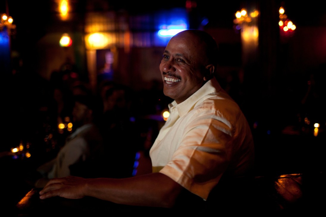 Yafet Habtu, co-owner of Club Alizé, smiling at a table in the dimly lit jazz club.