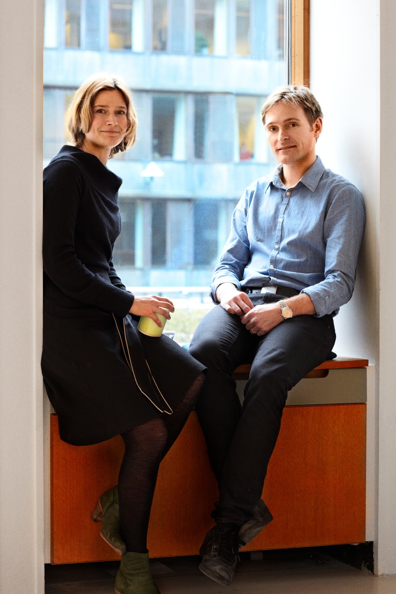 Two project managers, Runa Sabroe and Jakob Schjørring, sit on a wooden bench by a window at Mindlab in Copenhagen.