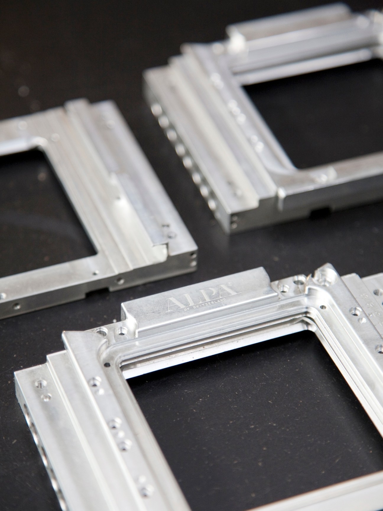 Close-up of newly-machined Alpa camera bodies showing aluminum and brass components with precision-drilled holes and mechanical details.