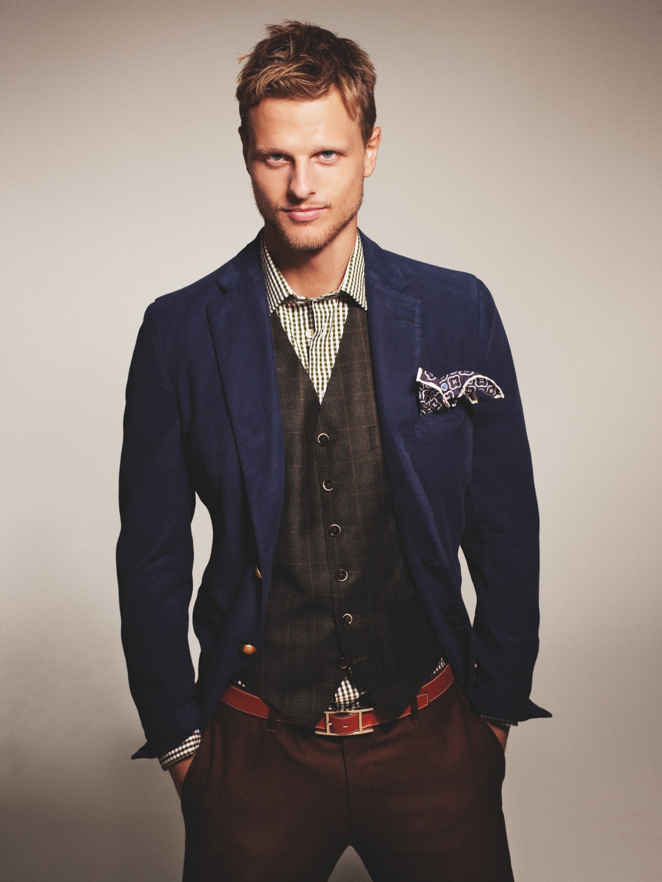 Man wearing navy blazer, brown waistcoat, and checkered shirt with patterned pochette.