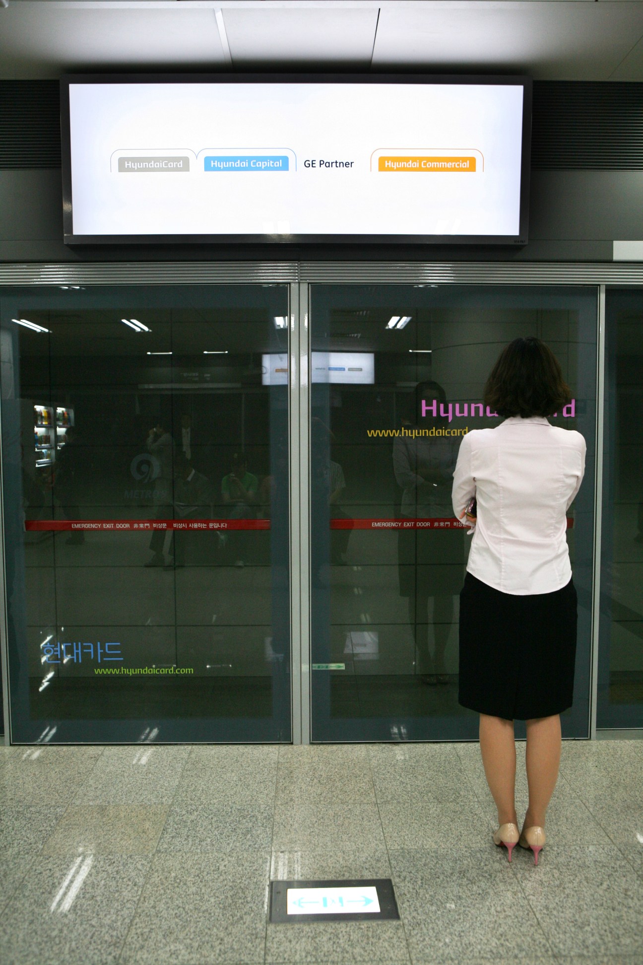 Woman viewing Hyundai Card minimal advertising on Seoul subway safety doors with logos on white background.