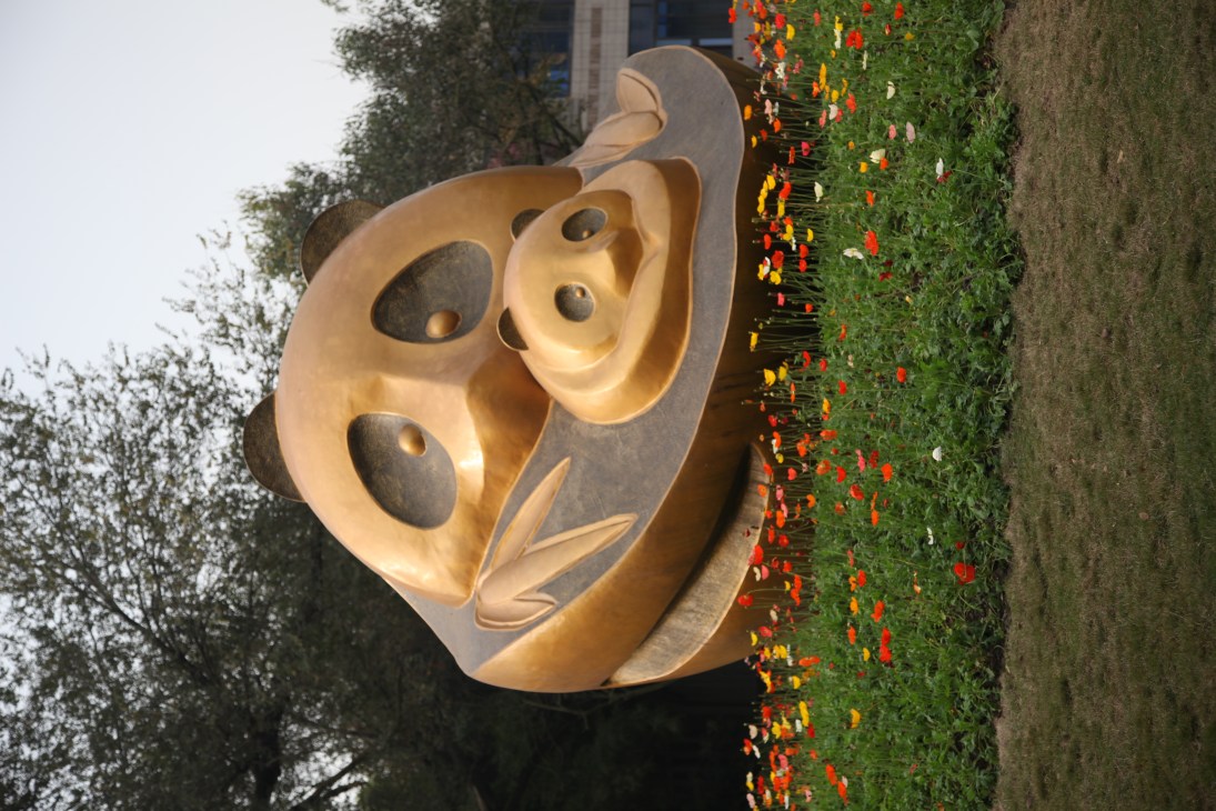 Large bronze panda sculpture at the Panda Base in Chengdu with flowering vines nearby.