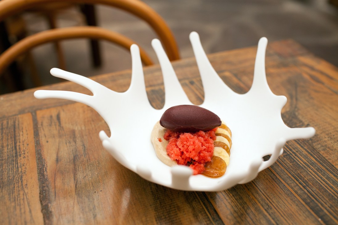 Artfully plated dish with red roe, dark sauce, and crispy garnish on white sculptural plate at Maní restaurant.