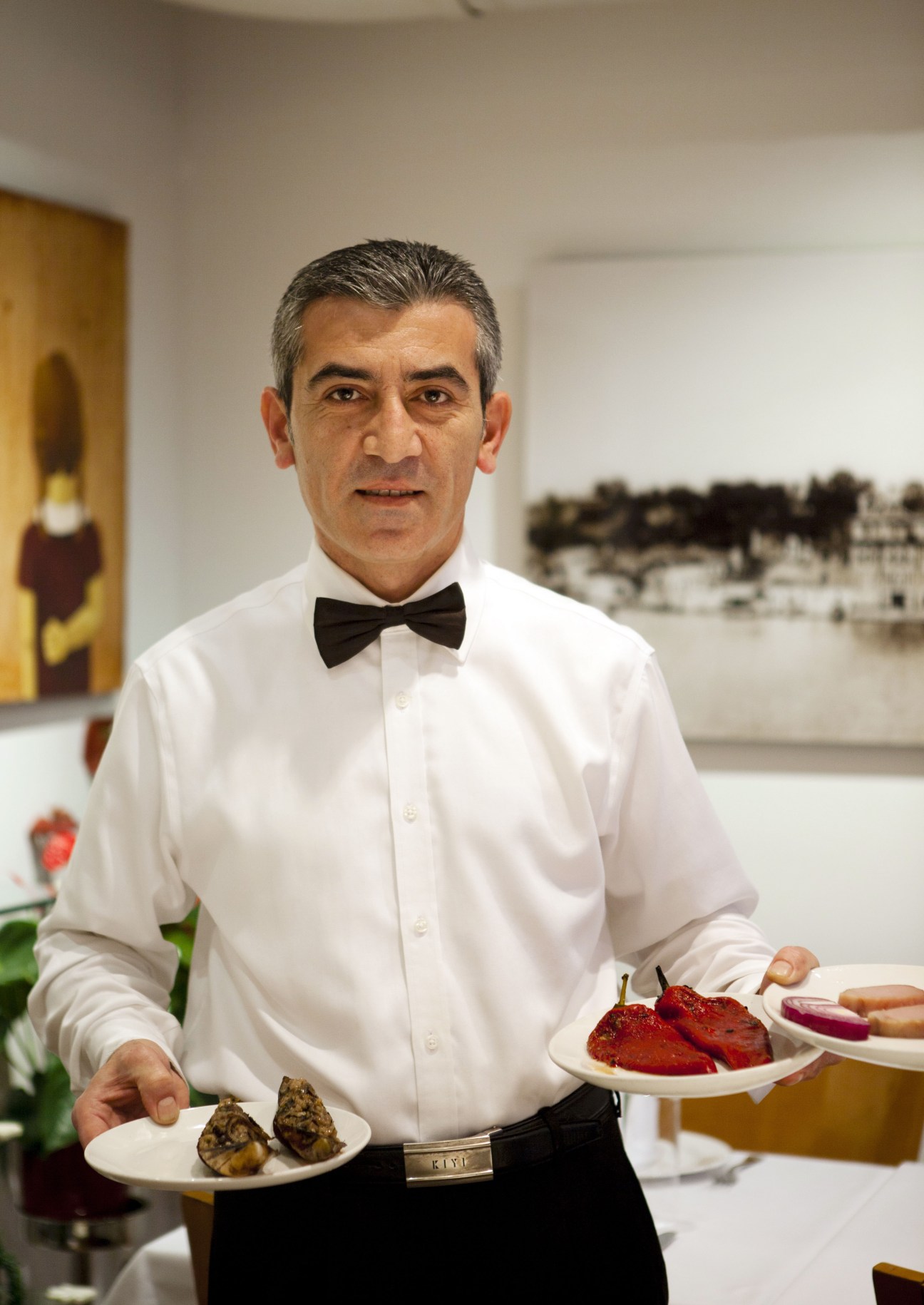 A waiter in formal attire holds plates of mezze dishes at Kiyi restaurant.