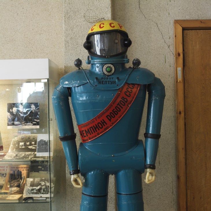 Blue Soviet robot with yellow helmet and red sash displayed in museum