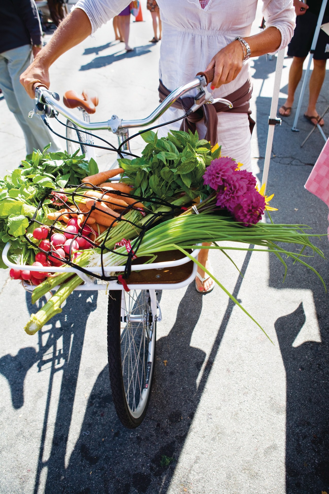 Person holding Globe LIVE bike loaded with fresh produce and flowers at farmers' market.