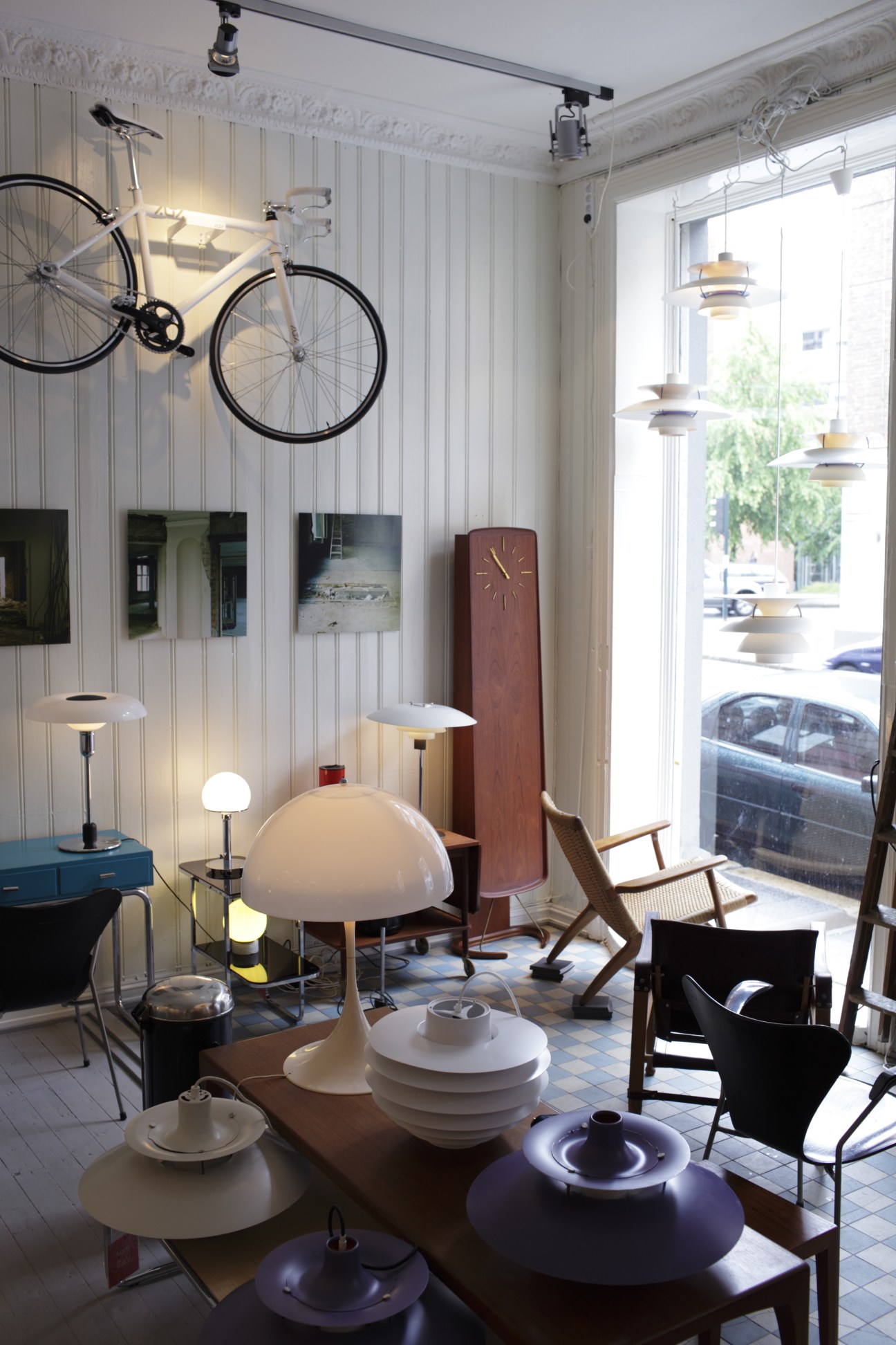 Interior of Cirka Design vintage shop displaying mid-century Scandinavian furniture, lamps, and a bicycle on white paneled walls.