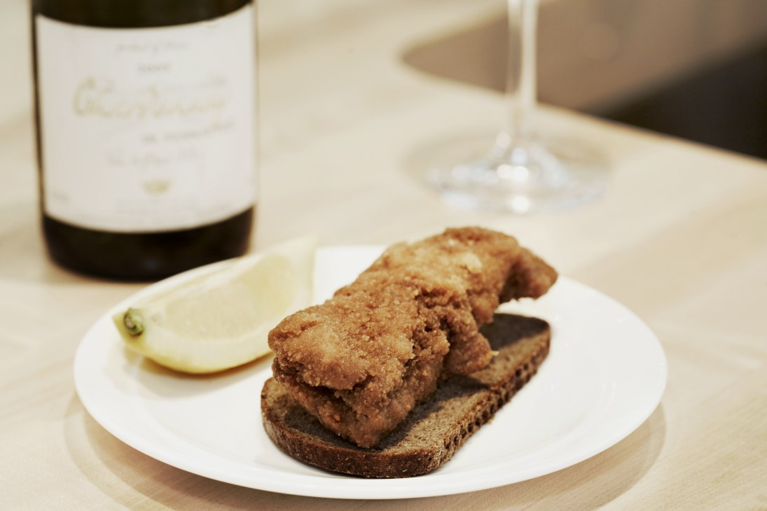 Pickled, fried herring smørrebrød on white plate with wine bottle nearby.