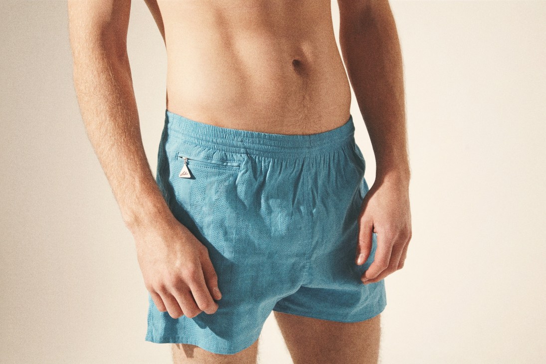 Man wearing light blue Lahco swim trunks with silver triangular tag on waistband.