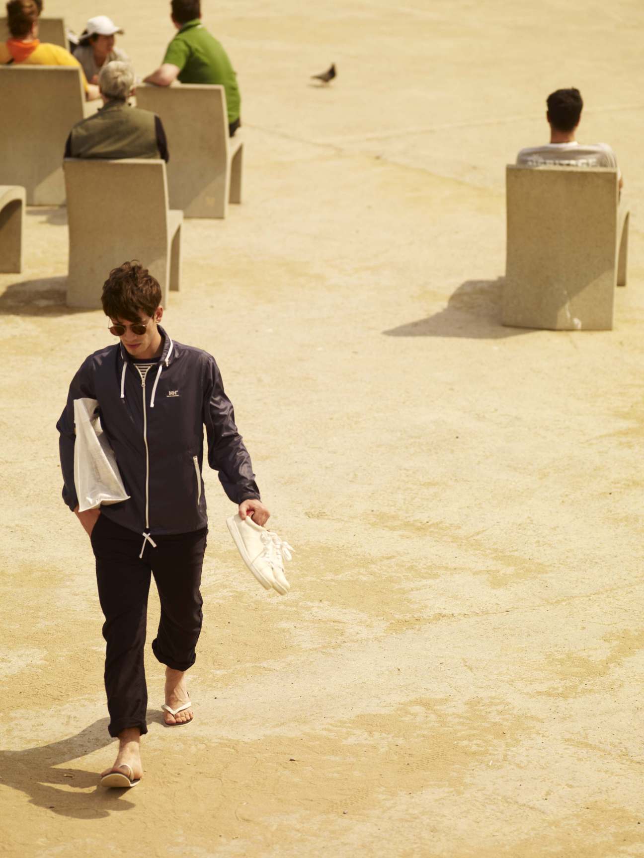 Man wearing Helly Hansen jacket and White Mountaineering trousers walks on beach sand.