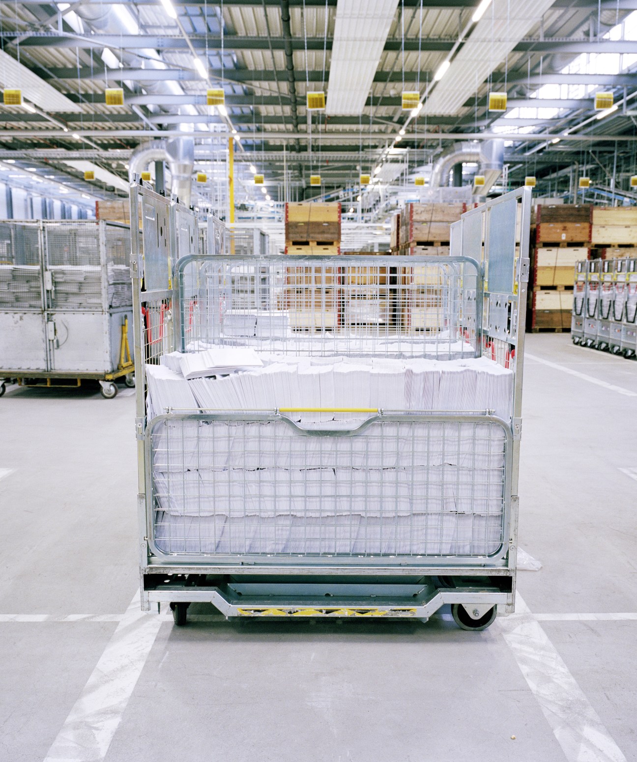A metal trolley filled with unsorted letters in a modern sorting facility with industrial ceiling.