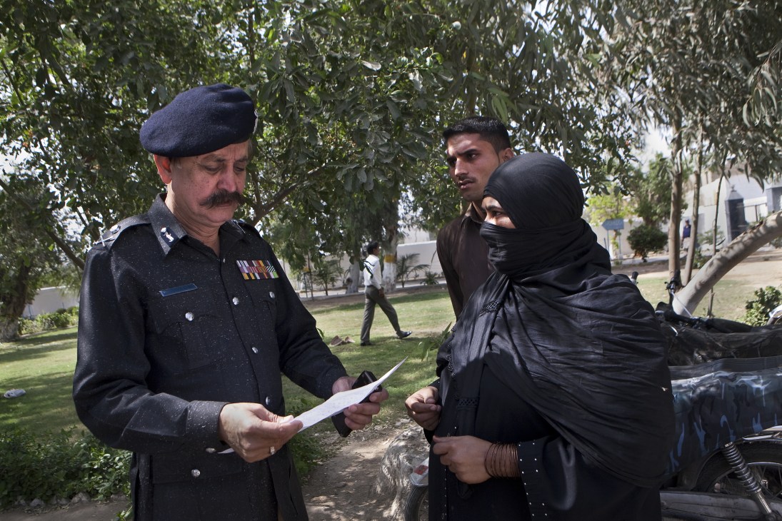 Waseem Ahmed, Karachi police chief, reads a letter outdoors with two civilians under tree shade.