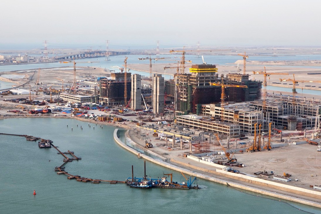 Aerial view of Al-Reem construction site with multiple cranes, unfinished buildings, and Saadiyat Bridge visible in the distance.