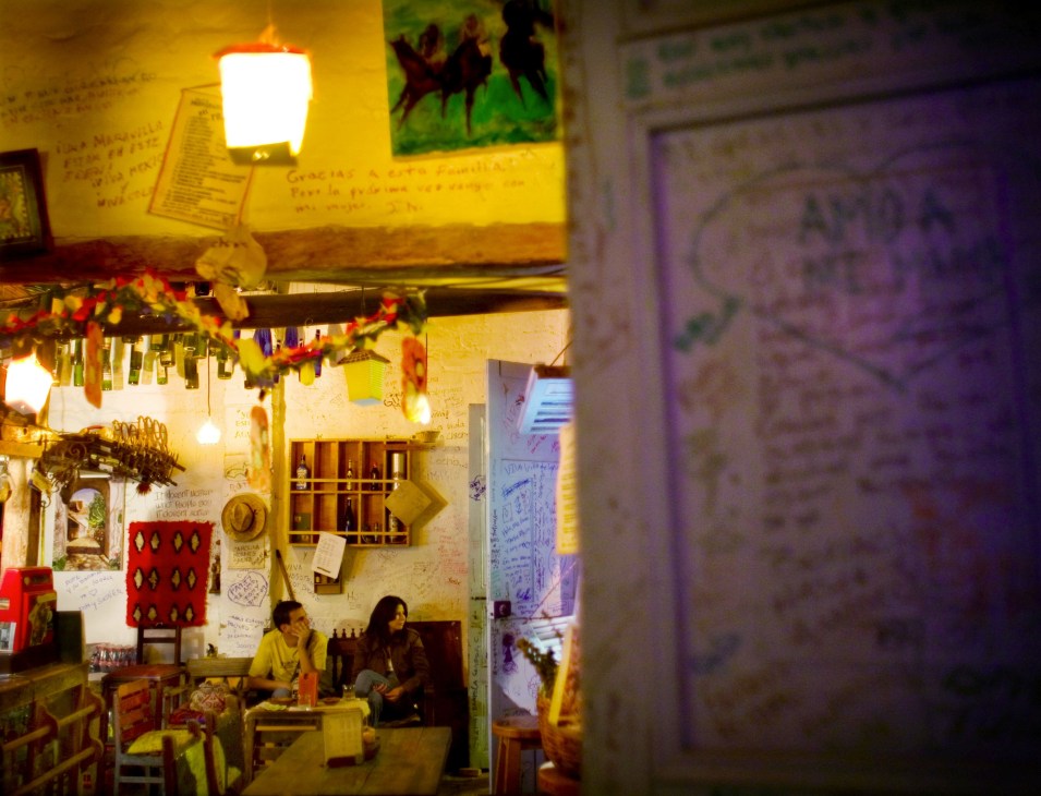Interior of Mr Coqui bar with warm yellow lighting, patrons seated, and decorated walls with handwritten messages and artwork.