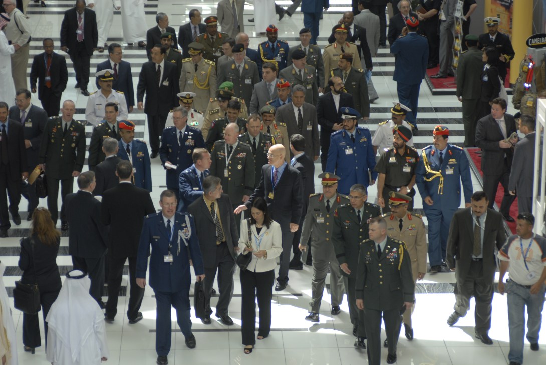 Senior military officials and government delegates walking through an indoor exhibition hall at IDEX.