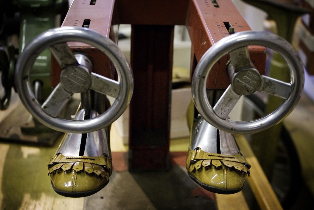 Two yellow leather women's shoes with metal buckle details clamped in a repair vise at Ermanno Alvisi's cobbler shop.