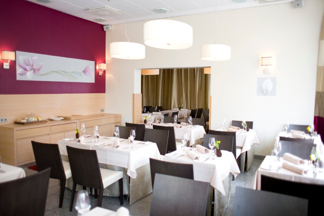 Modern restaurant dining room with magenta accent wall, pendant lighting, and white tablecloth tables.