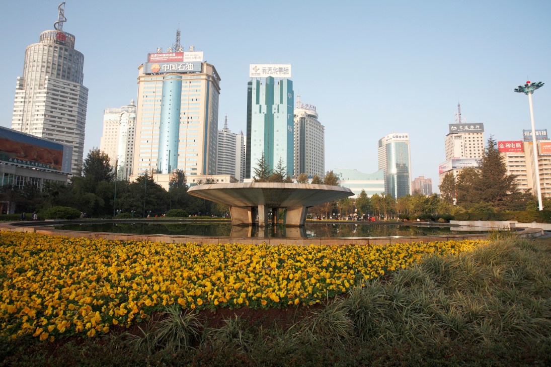 Fountain in Dong Feng Square with yellow flowers, modern buildings and clear blue sky in downtown Kunming.