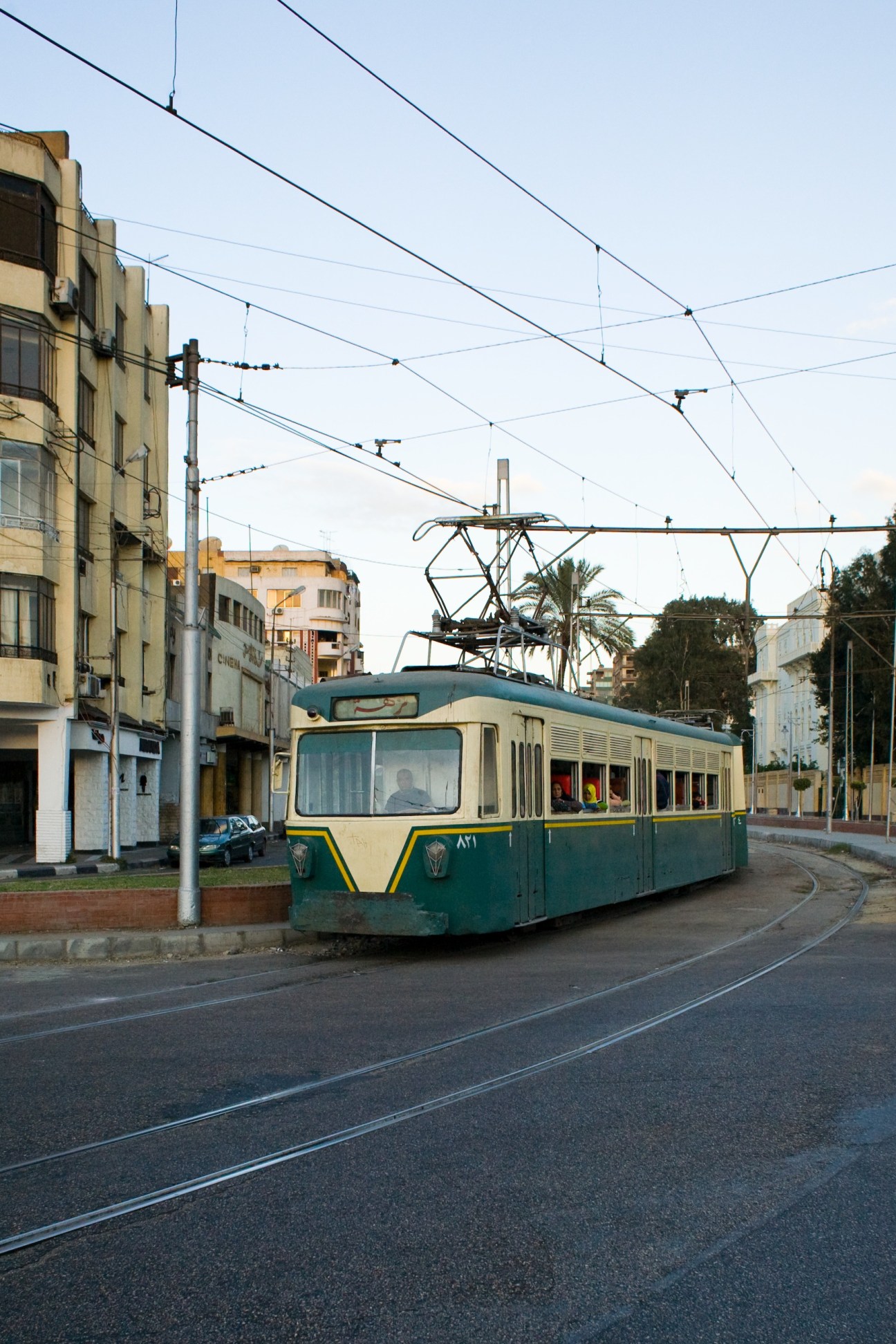 A vintage green and cream tram travels along tracks through an El Korba street lined with early 20th-century buildings.