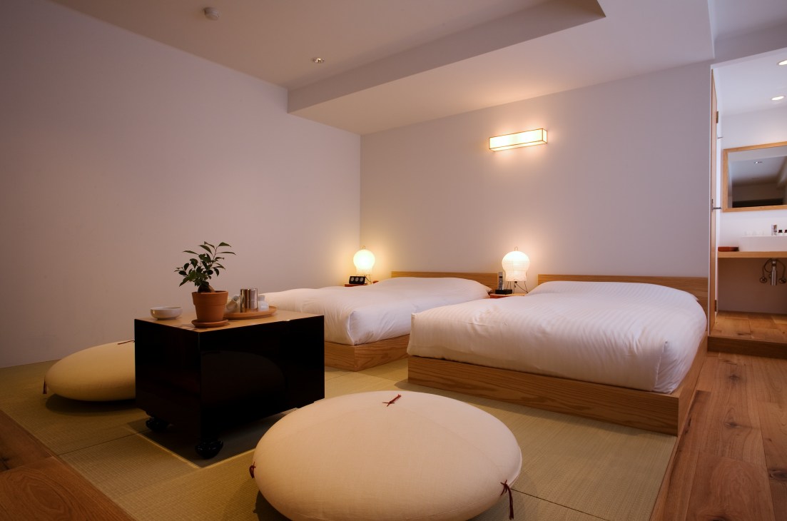 Minimalist contemporary bedroom with two low wooden beds, round cushioned seating, and soft lighting designed by Kaname Okajima.