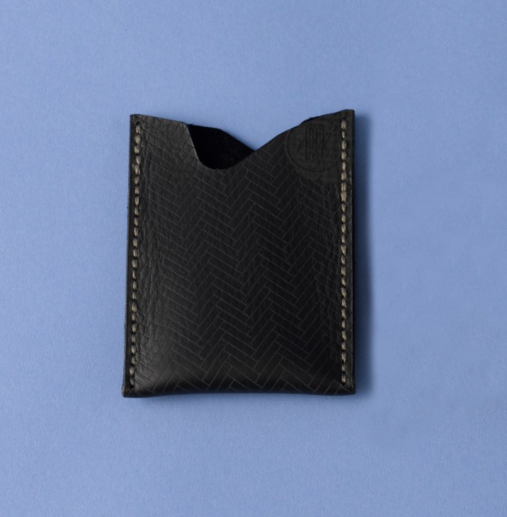 Black leather wallet with herringbone texture and contrasting topstitching on light blue background.