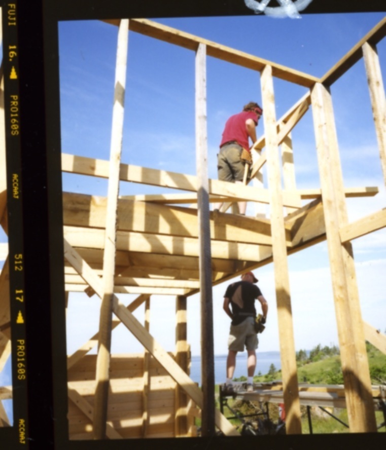 Two construction workers building wooden frame structure at upper site with clear blue sky.