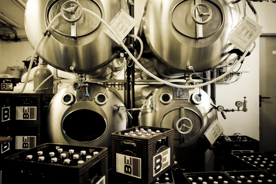 Large stainless steel fermentation vats with control panels and piping in a brewery.