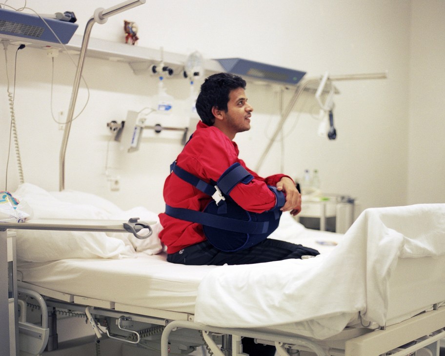 Ahmed Ahmed Hussein from Egypt sits on a hospital bed wearing a red jacket and blue support brace.