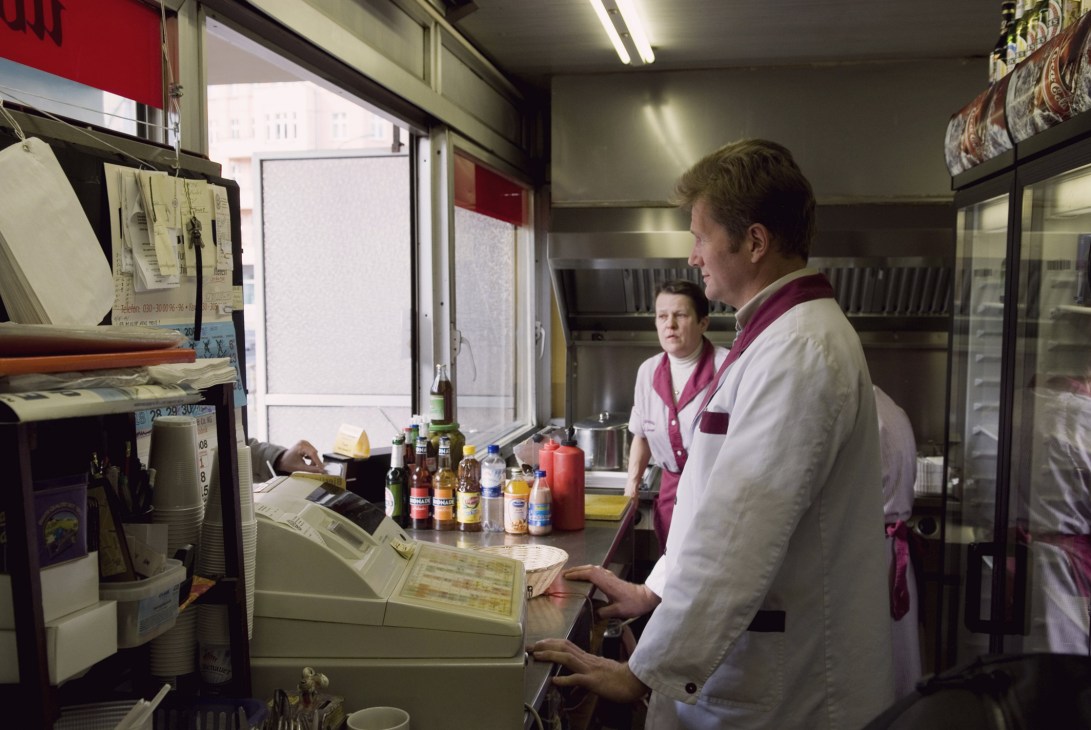 Staff members at Konnopke's sausage stand in Berlin working at the counter with condiments displayed.